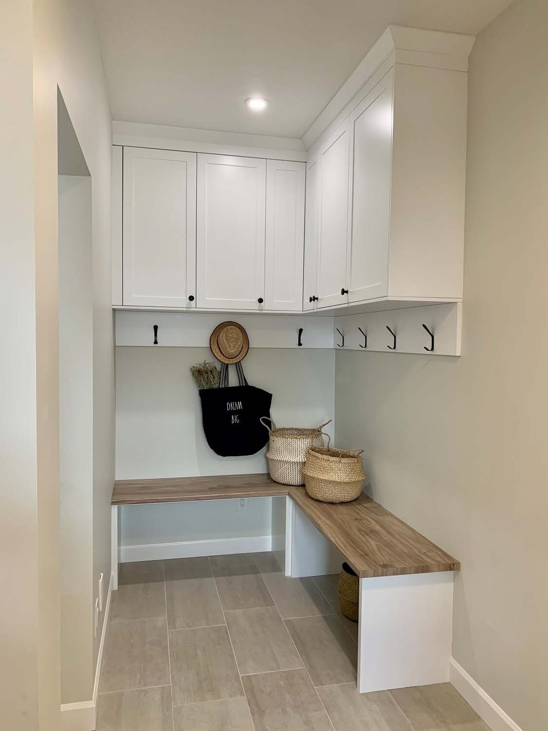 White mudroom nook with a wood bench, coat hooks, and upper cabinets